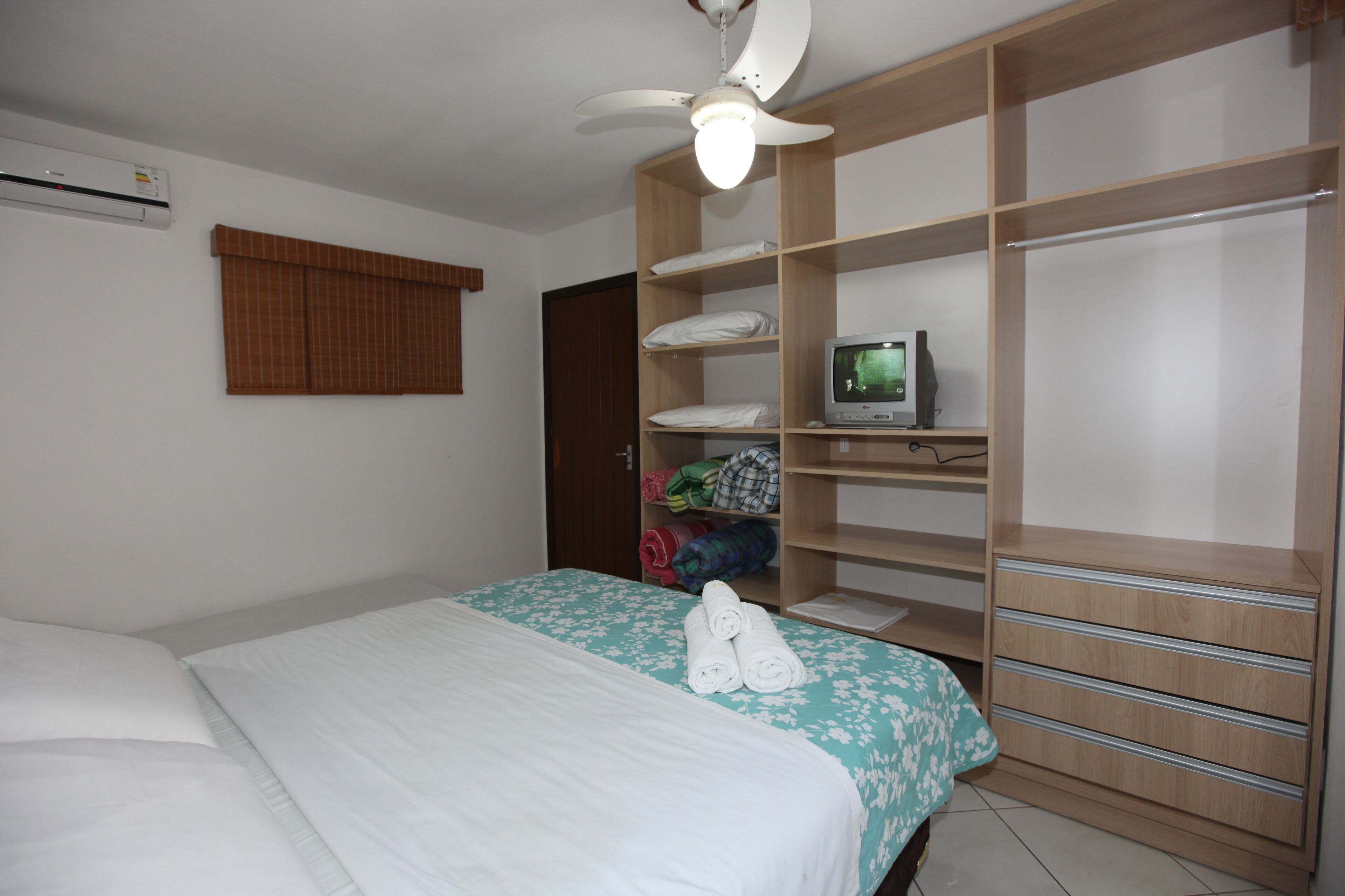 A bedroom with a bed, a wardrobe, a television, and an air conditioner.