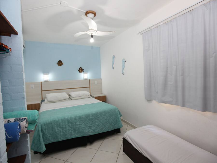 A bedroom with a bed, a bedside table, a nightstand, a ceiling fan, and a window with curtains.