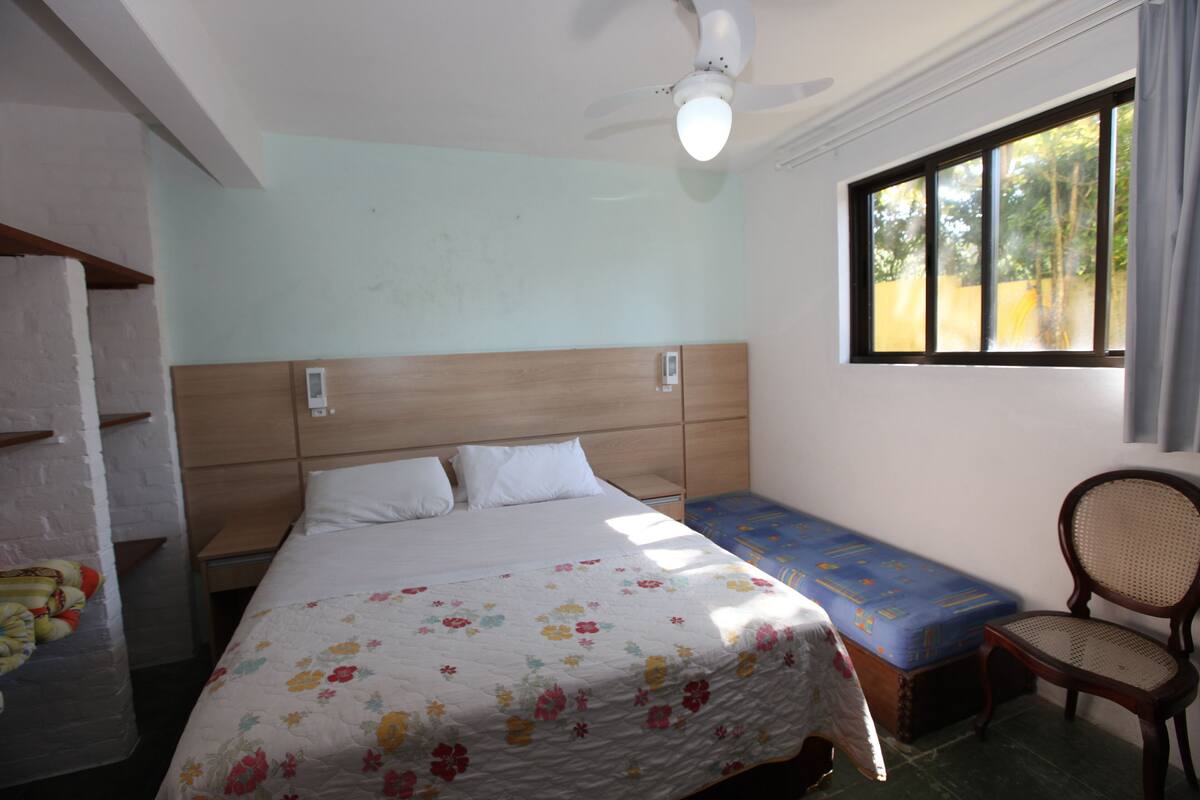 Ein Schlafzimmer mit Bett, Nachttisch, Stuhl, Fenster und Deckenventilator.