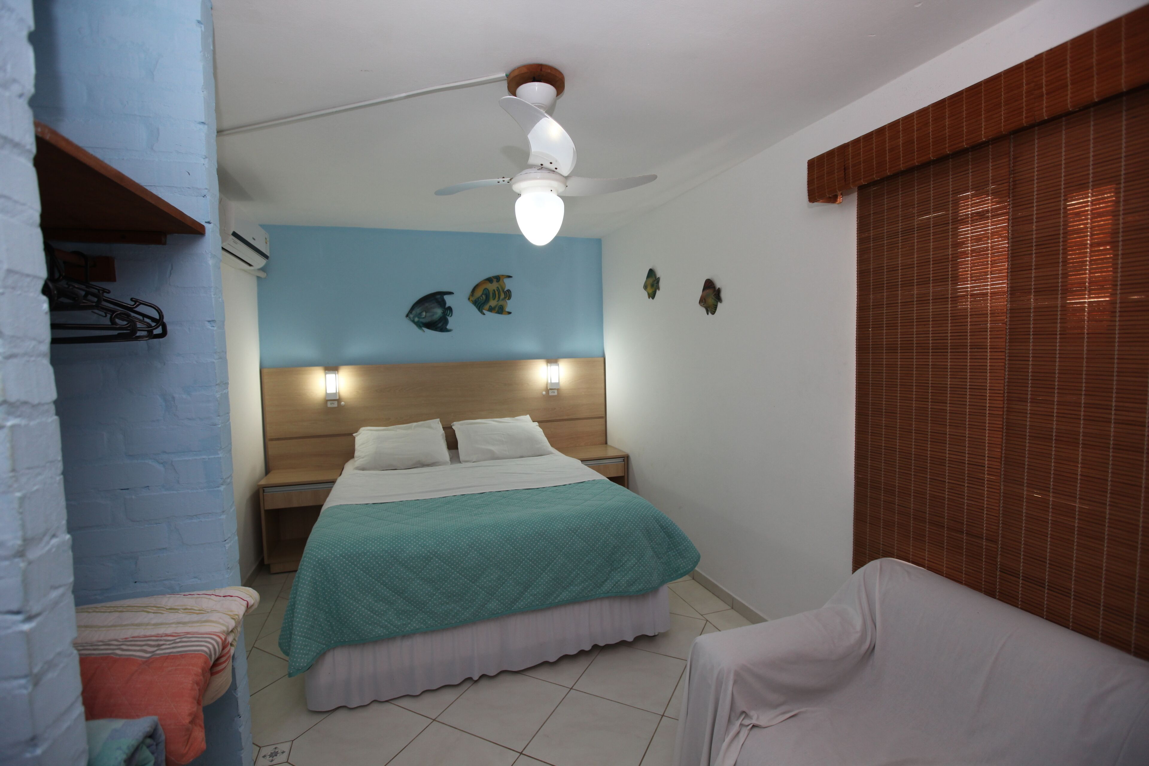 A bedroom with a bed, bedside tables, a ceiling fan, wall-mounted lights, and a window with blinds.