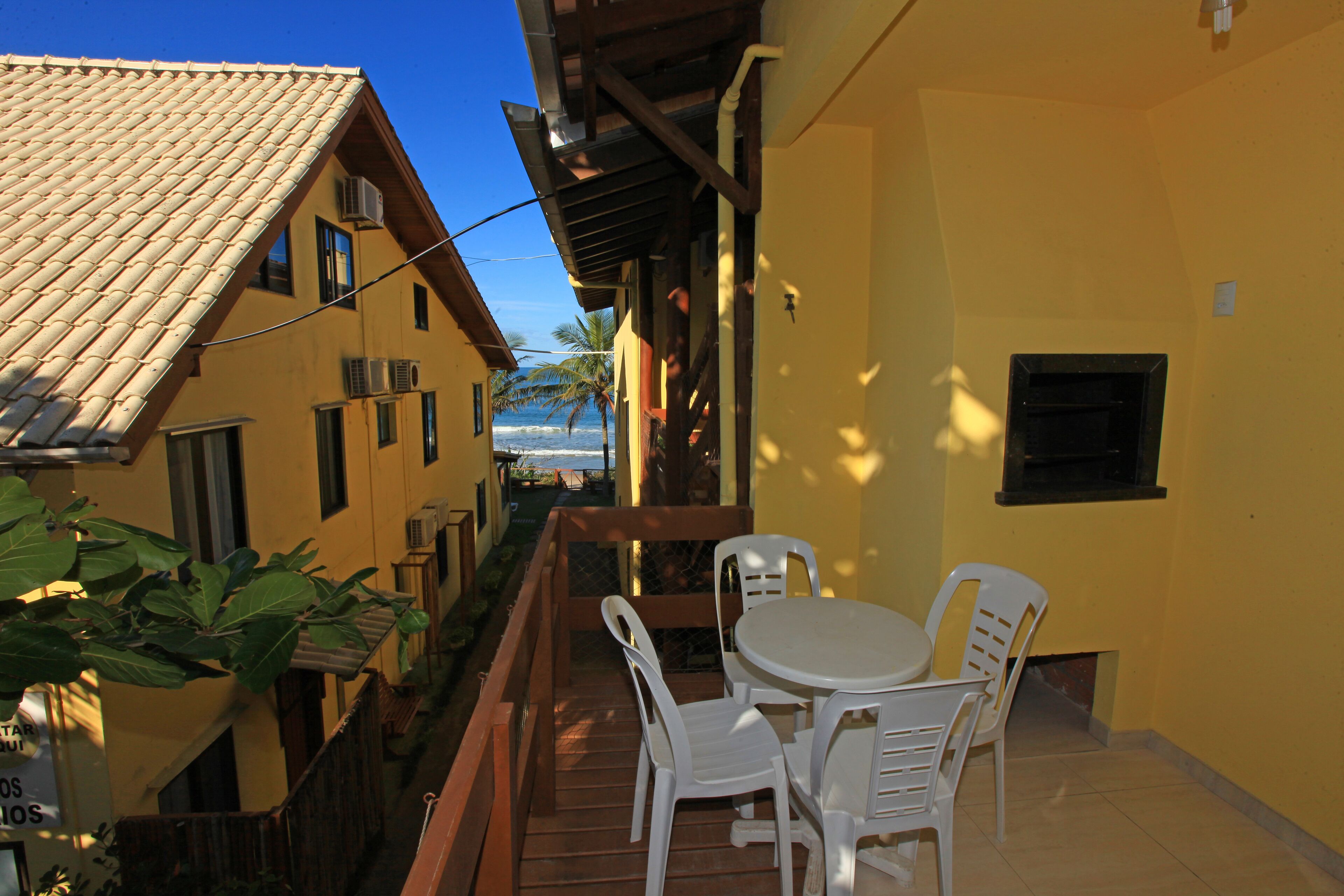 A balcony with a wooden floor, white plastic chairs, and a small round table.
