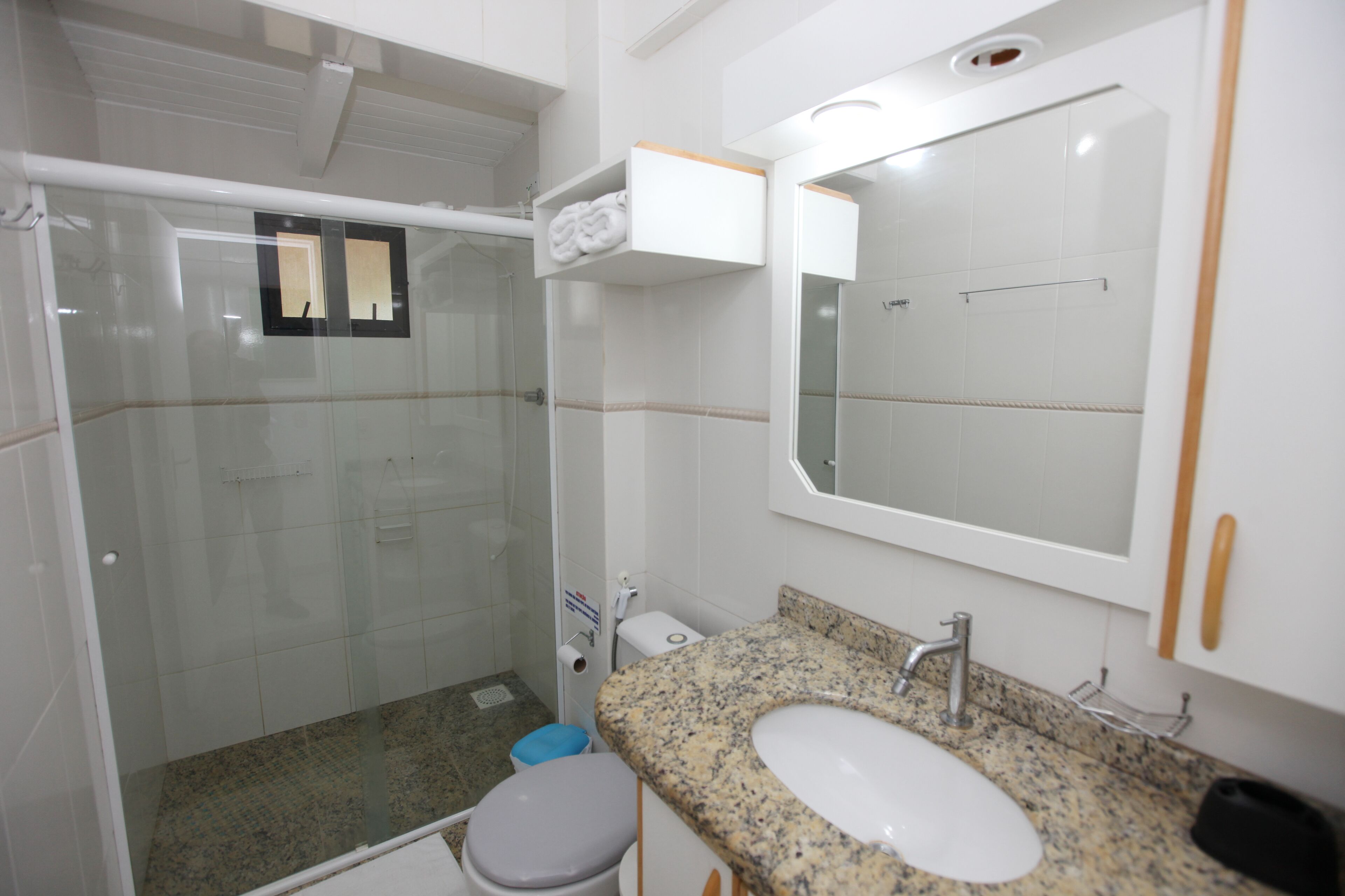 A bathroom with a glass shower enclosure, a granite countertop sink, and a white toilet.