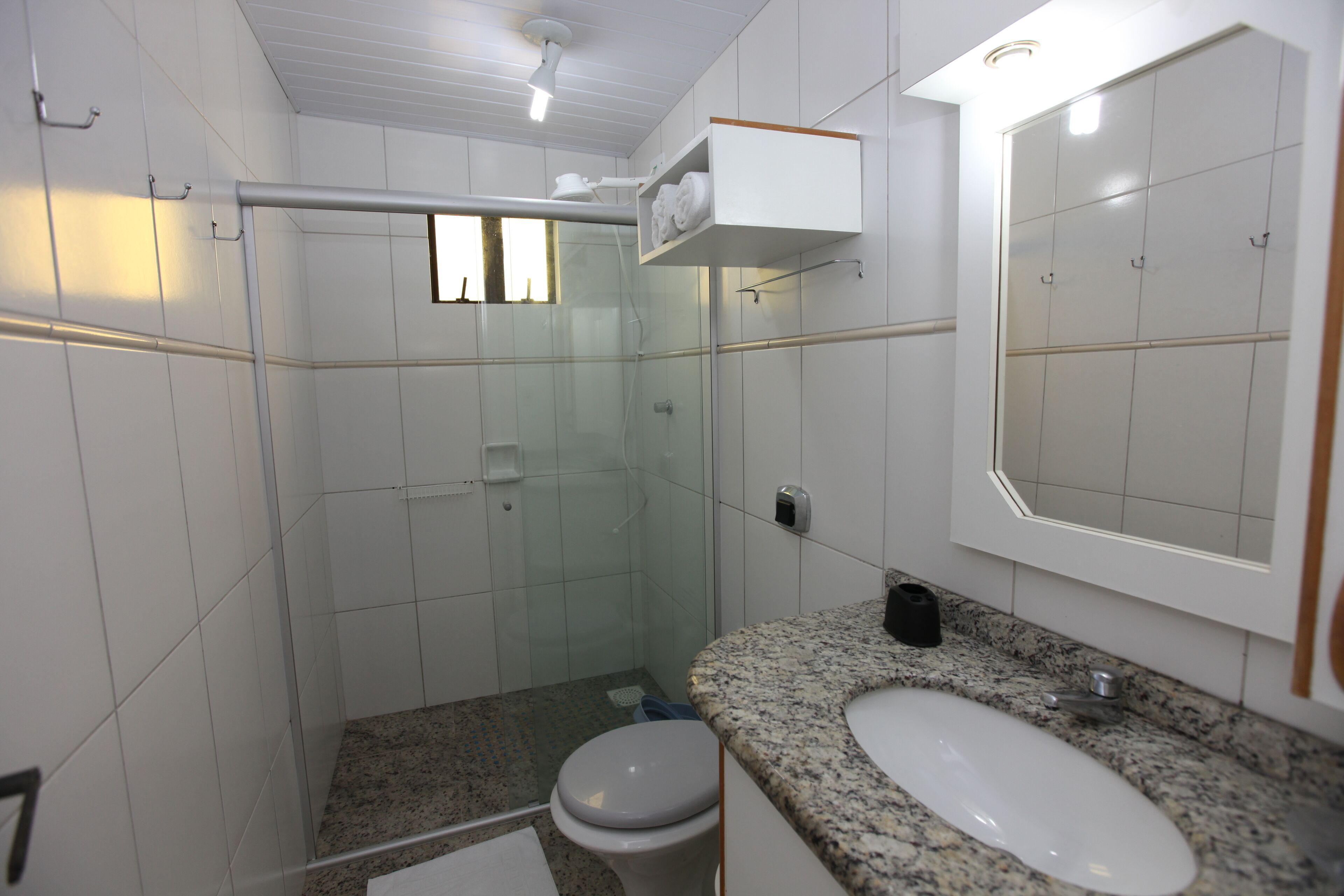 Uma casa de banho com cabine de duche em vidro, sanita branca, bancada de granito e espelho grande.