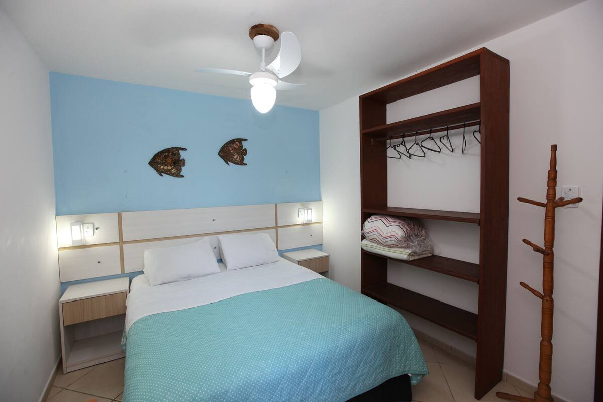 Ein Schlafzimmer mit Bett, Nachttisch, Kleiderschrank und Deckenventilator.