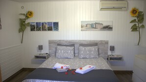 Een netjes opgemaakt slaapkamer met een bed, twee nachtkastjes, een wandairconditioner en twee zonnebloemen.