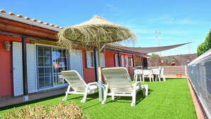 Een terras met witte lounge fauteuils, een rieten zonnescherm en een kleine tafel.