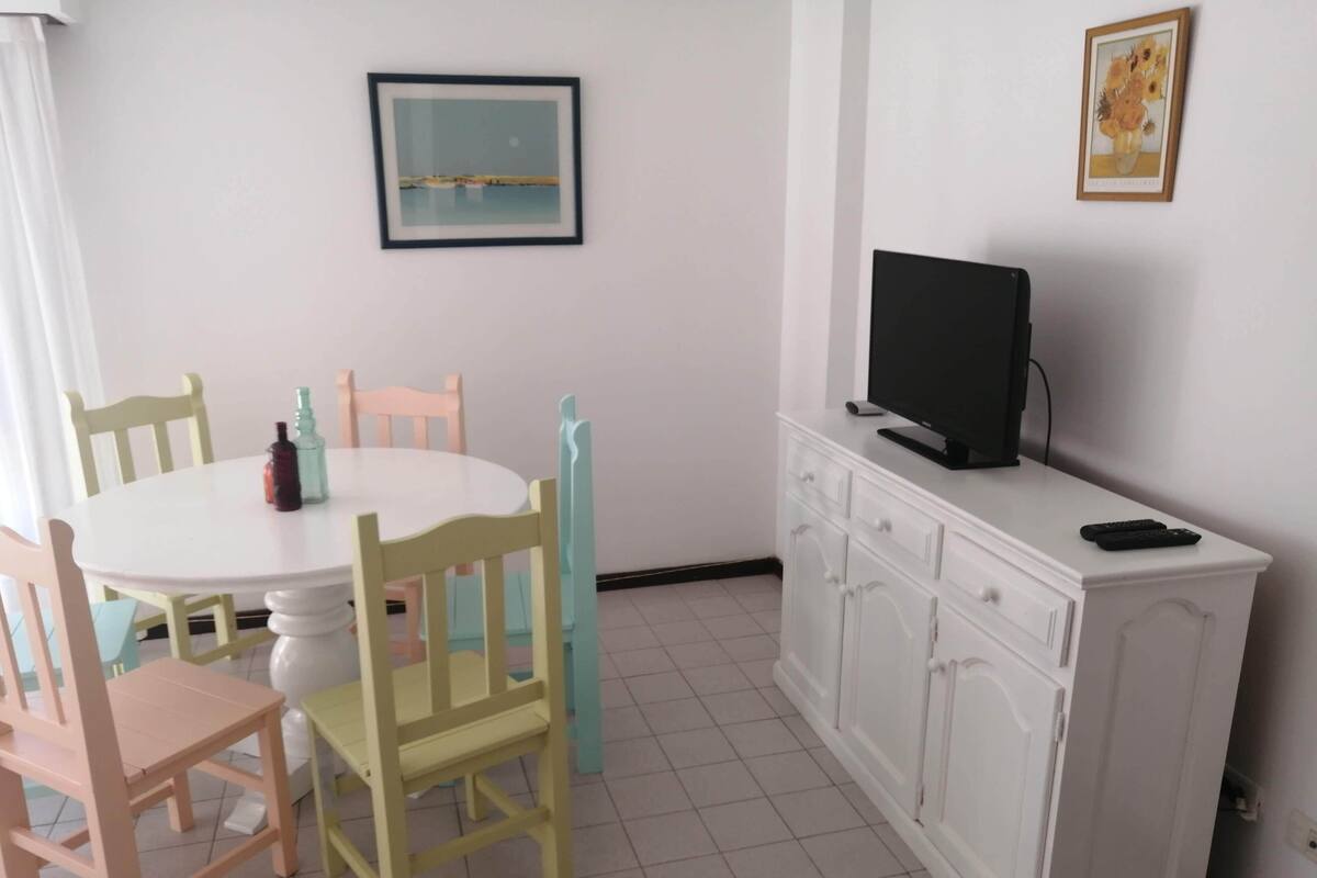 A dining area with a round table, chairs, a television on a cabinet, and framed artwork on the walls.