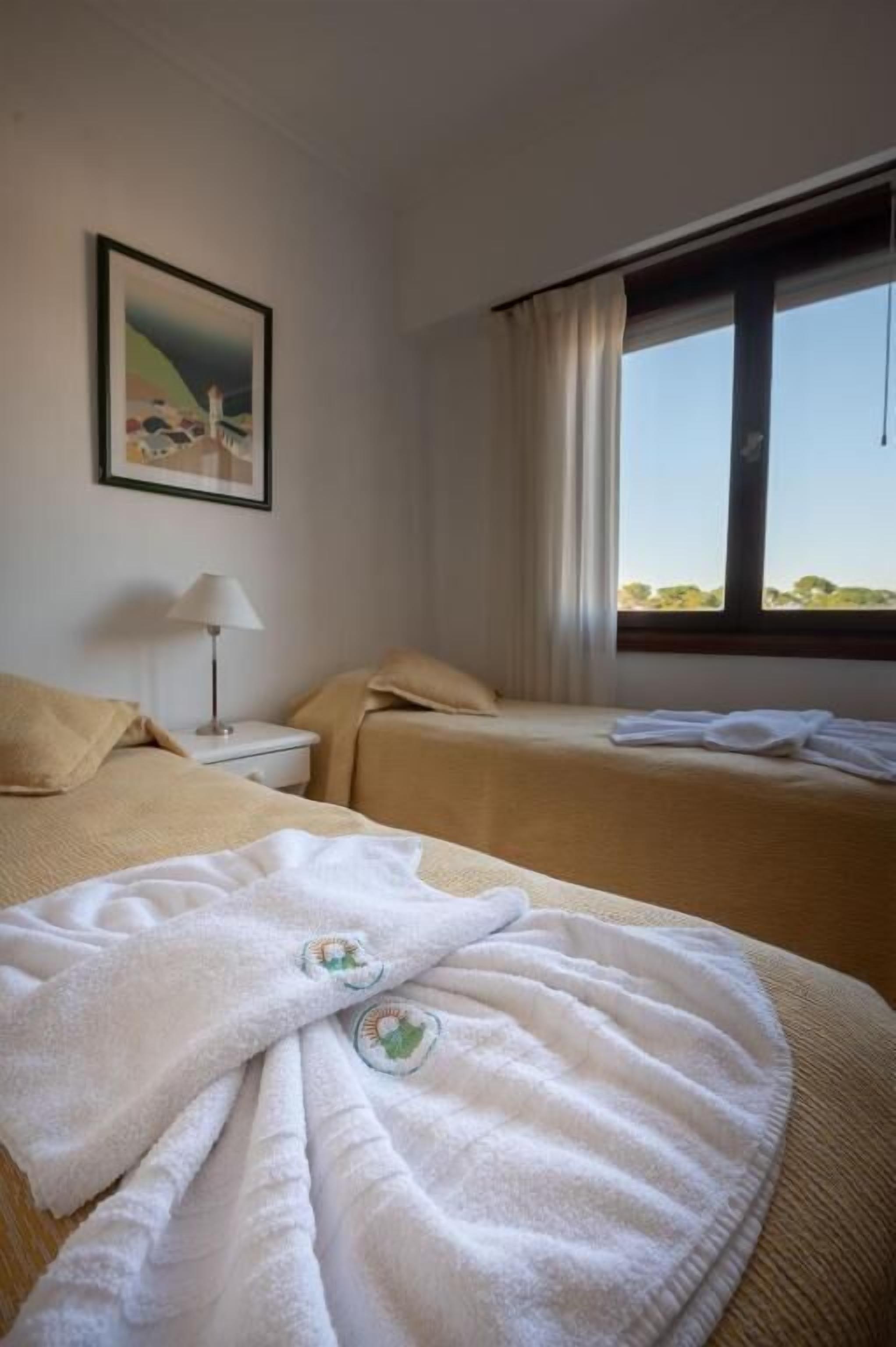 Quarto de hotel com duas camas, uma mesa de cabeceira, uma luminária e um quadro na parede.