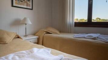 Quarto de hotel com duas camas, uma mesa de cabeceira, uma luminária e um quadro na parede.