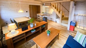 A modern interior with a wooden floor, a dining area with a table and chairs, a sofa, a staircase, and a kitchen area. - Baan Hakuba (Hakuba)