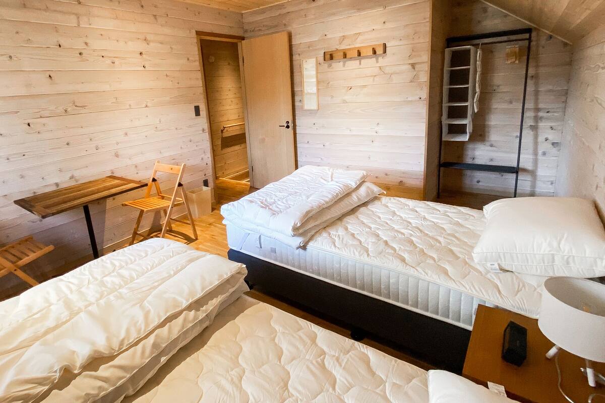 Una habitación tipo cabaña de madera con dos camas, un escritorio y una escalera.