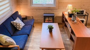 A cozy room with a blue sofa, a wooden table, a small stove, and a window with blinds. - Baan Hakuba (Hakuba)