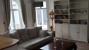 Una sala de estar con un sofá modular, una mesa de centro, una estantería y una ventana con cortinas.