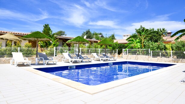 A swimming pool with lounge chairs and umbrellas, surrounded by a fence and greenery. - OFFER 2020 VILLA CLAJESSI - 4 PERSONS (Albufeira)