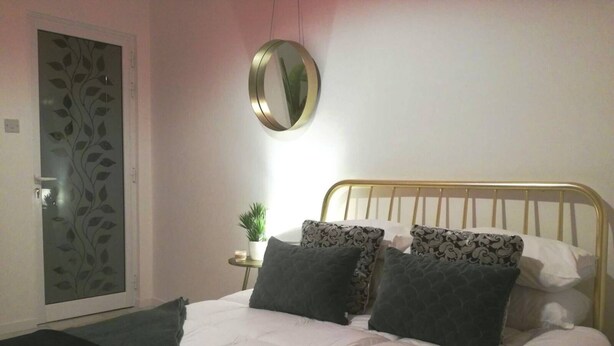 A bedroom with a bed, a round mirror, a small table with a plant, and a decorative door. - Private Room With Ensuite Groundfloor (Luqa)