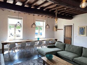 A dining area with a wooden table and chairs, a green sofa, and pendant lights. - Exclusive authentic mansion (16p) near Maastricht (Eijsden)