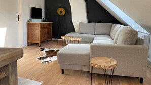 Een moderne loft met schuine plafonds, een grijze hoekbank, een houten kast en een kleden van koeienhuid.