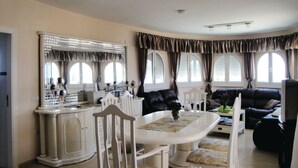 Un coin repas avec une table et des chaises blanches, un grand miroir et un canapé en cuir noir.