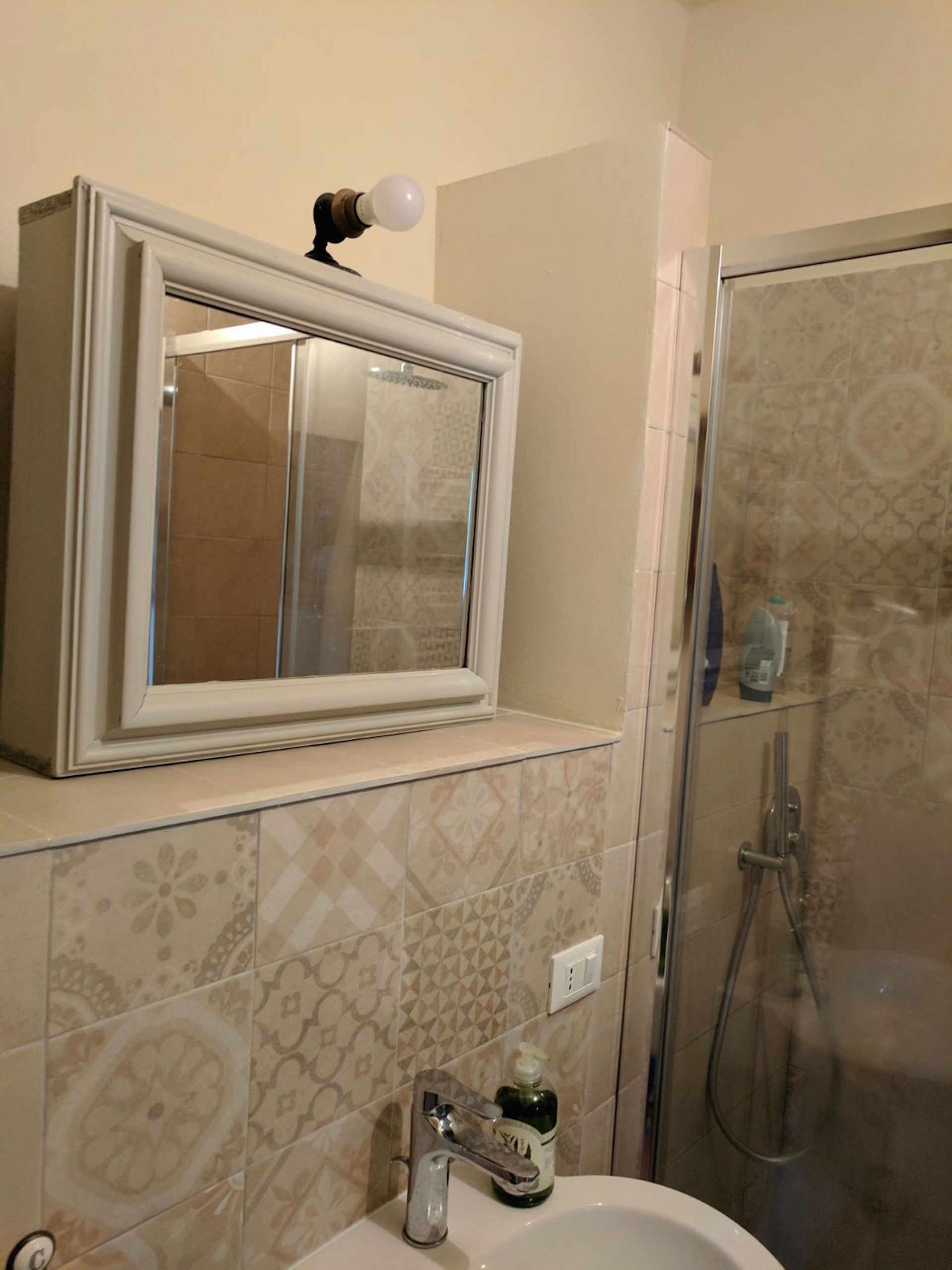A bathroom with a large mirror, a sink with a soap dispenser, and a shower area.
