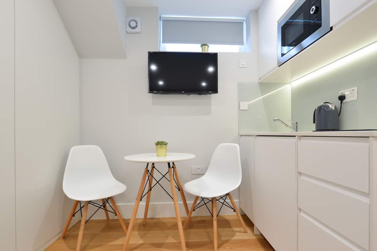 A compact kitchen with a flat-screen TV, white cabinets, and a small dining table with two chairs.