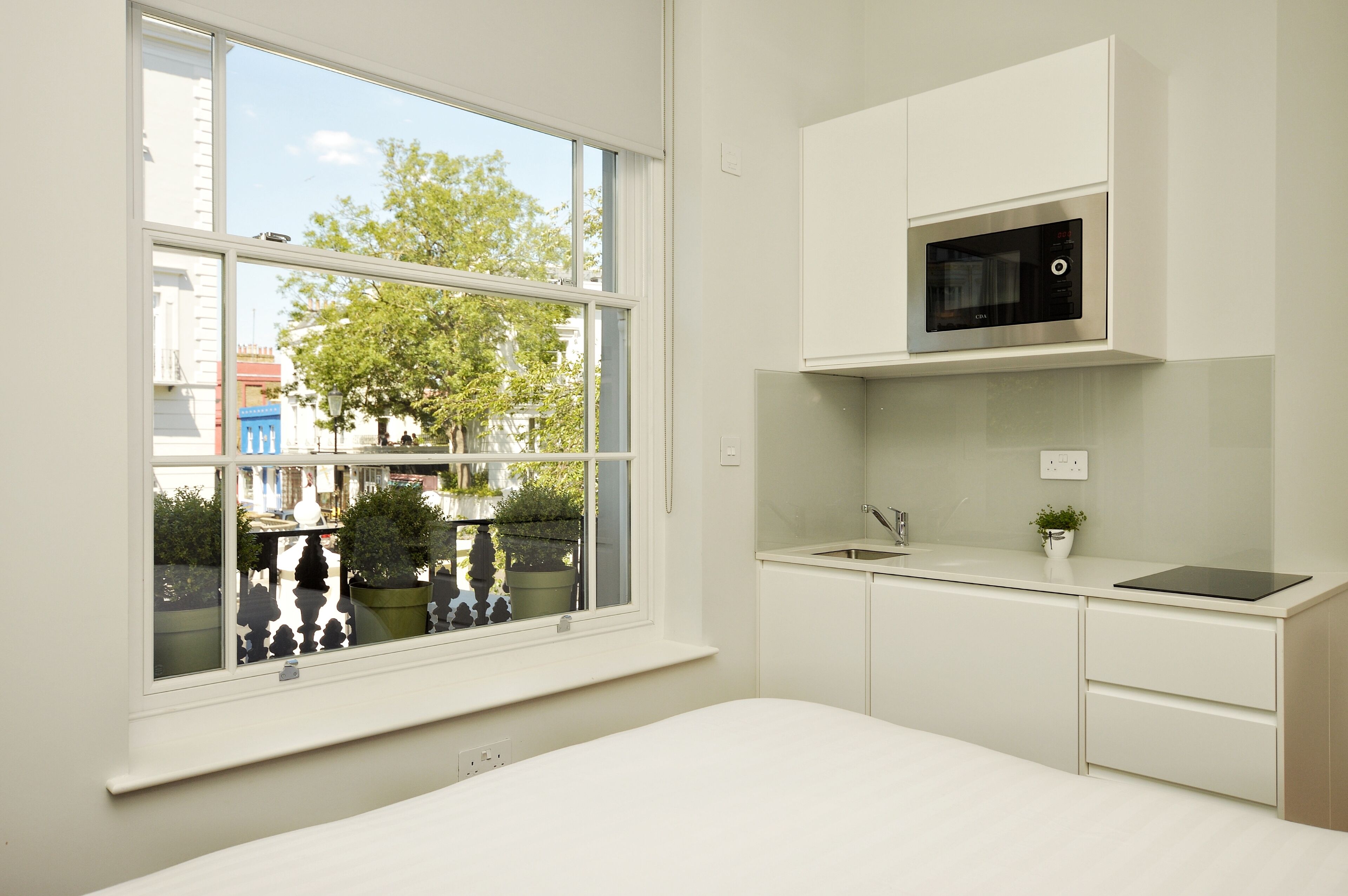 A modern kitchen with white cabinetry, a built-in microwave, and a window overlooking a street with trees and buildings.