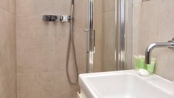 A modern shower with a handheld showerhead and a handheld hose, a white sink with a soap dispenser, and a mirror on the wall.