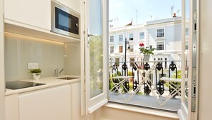 Eine moderne Küche mit integriertem Mikrowellenherd, Spüle und Fenster mit Blick auf einen Balkon, der mit einem Geländer und Topfpflanzen ausgestattet ist.