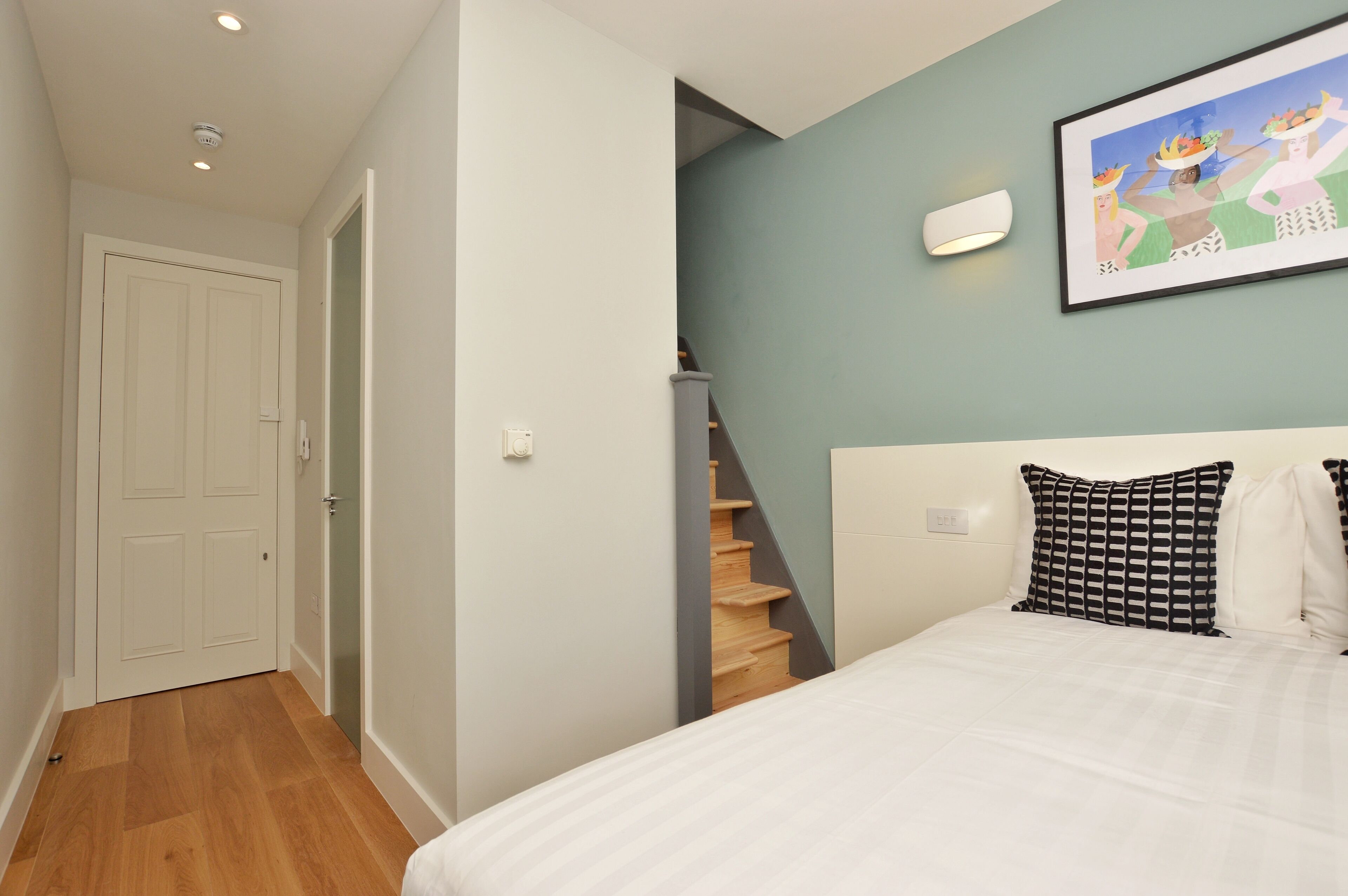 A bedroom with a bed, a staircase, a door, and a wall-mounted light fixture.