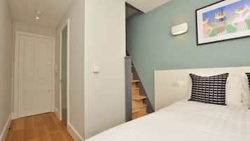 A bedroom with a bed, a staircase, a door, and a wall-mounted light fixture.