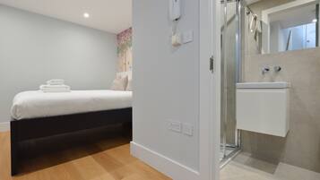 Un dormitorio moderno con cama, mesita de noche, zona de ducha y baño con lavabo y espejo.