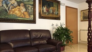 A living room with a brown leather sofa, two framed paintings, a potted plant, and a wooden floor. - Venice Mestre Tourist Accommodation, Quiet Room With Wifi and Free Parking (Mestre)