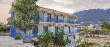 A multi-story building with balconies, a tree in front, and mountains in the background.