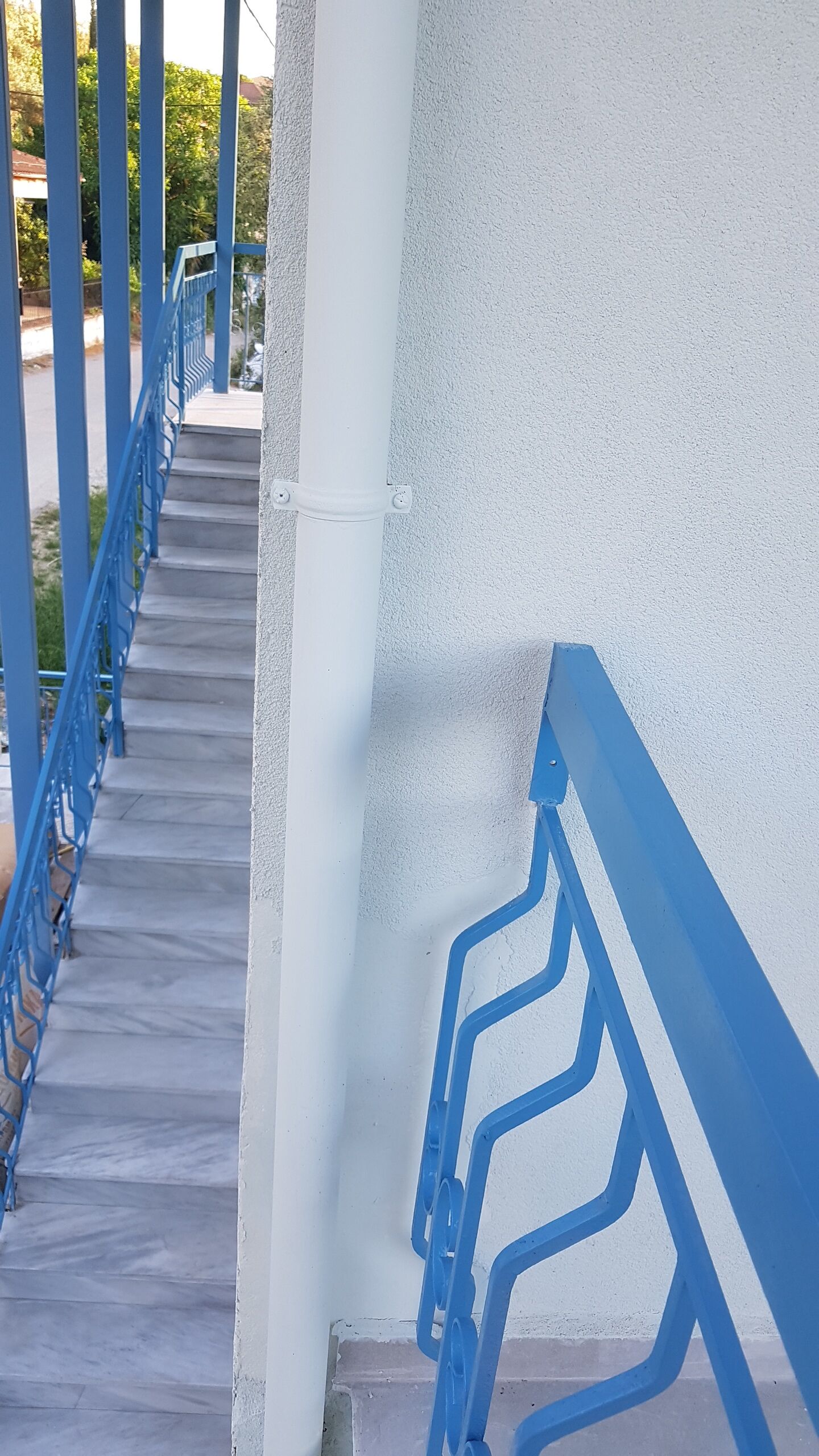 Un escalier en béton avec des rampes bleues menant à un mur blanc.