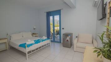 A bedroom with a bed, a chair, a small table, a radiator, and a door leading to an outdoor area.