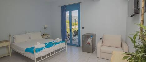 A bedroom with a bed, a chair, a small table, a radiator, and a door leading to an outdoor area.