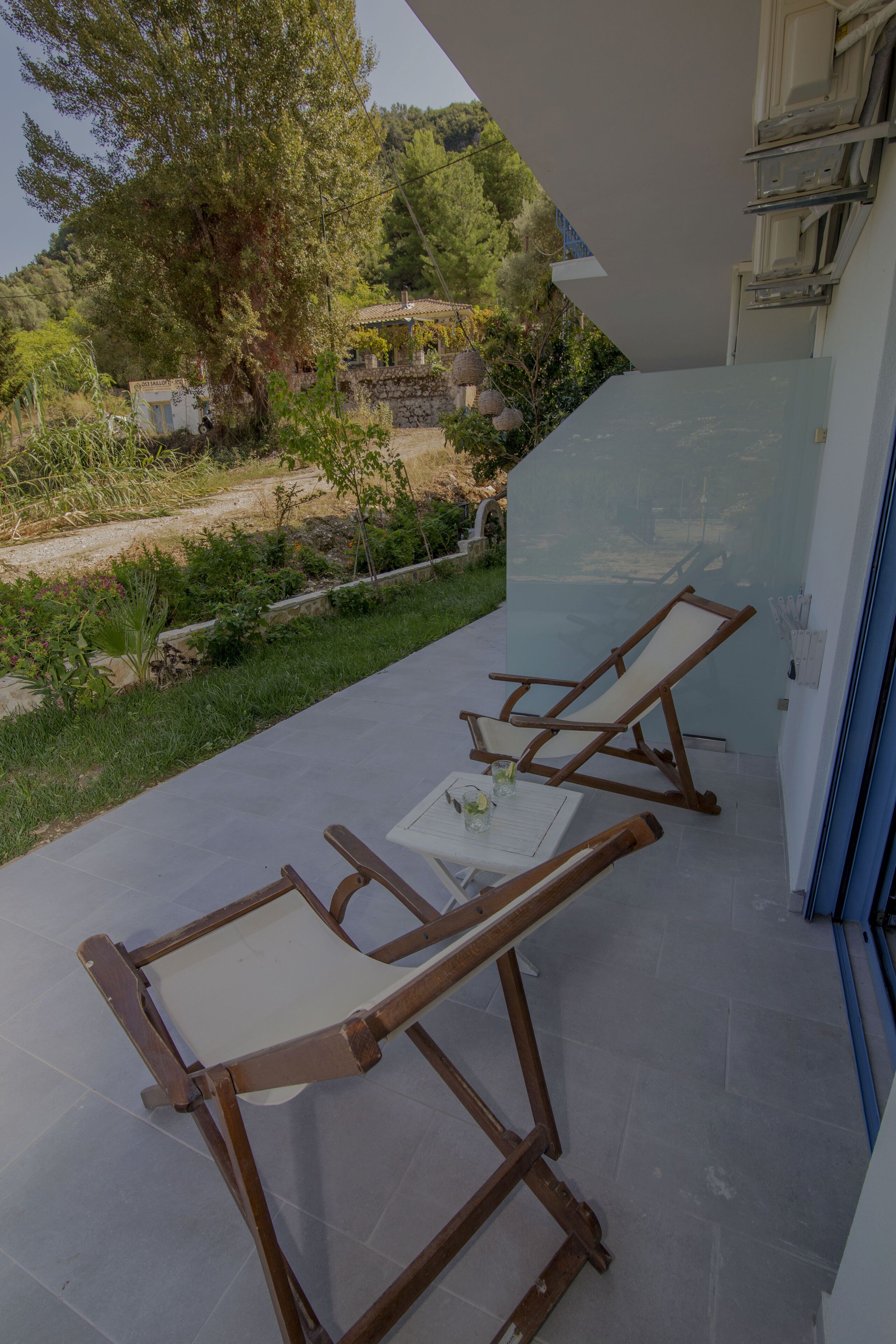 A balcony with two wooden lounge chairs and a small table, overlooking a garden and trees.