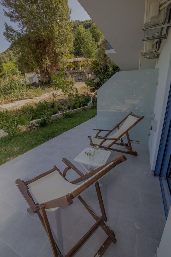 A balcony with two wooden lounge chairs and a small table, overlooking a garden and trees.