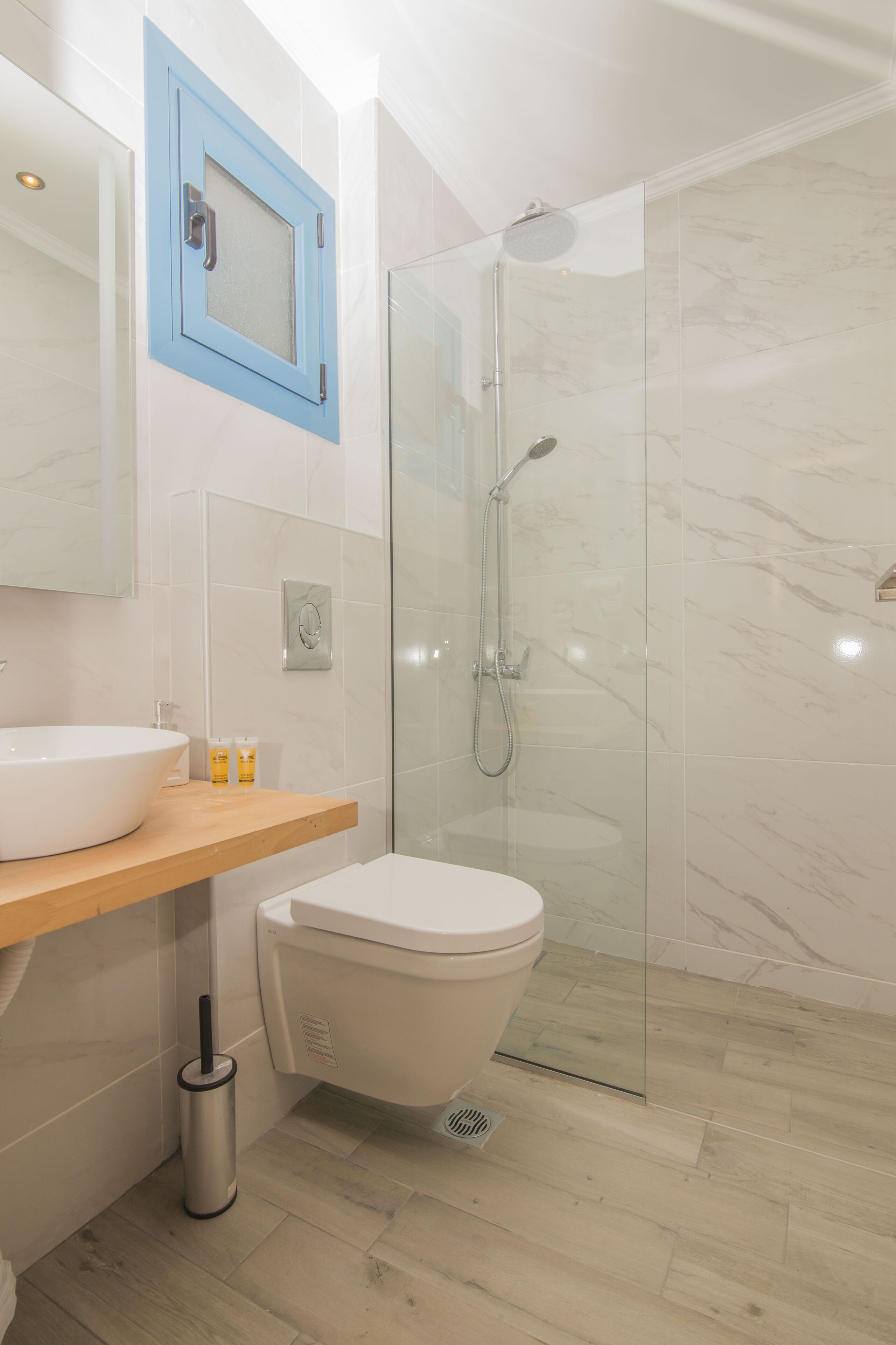 A modern bathroom with a glass-enclosed shower, a white toilet, and a wooden vanity with a large sink.