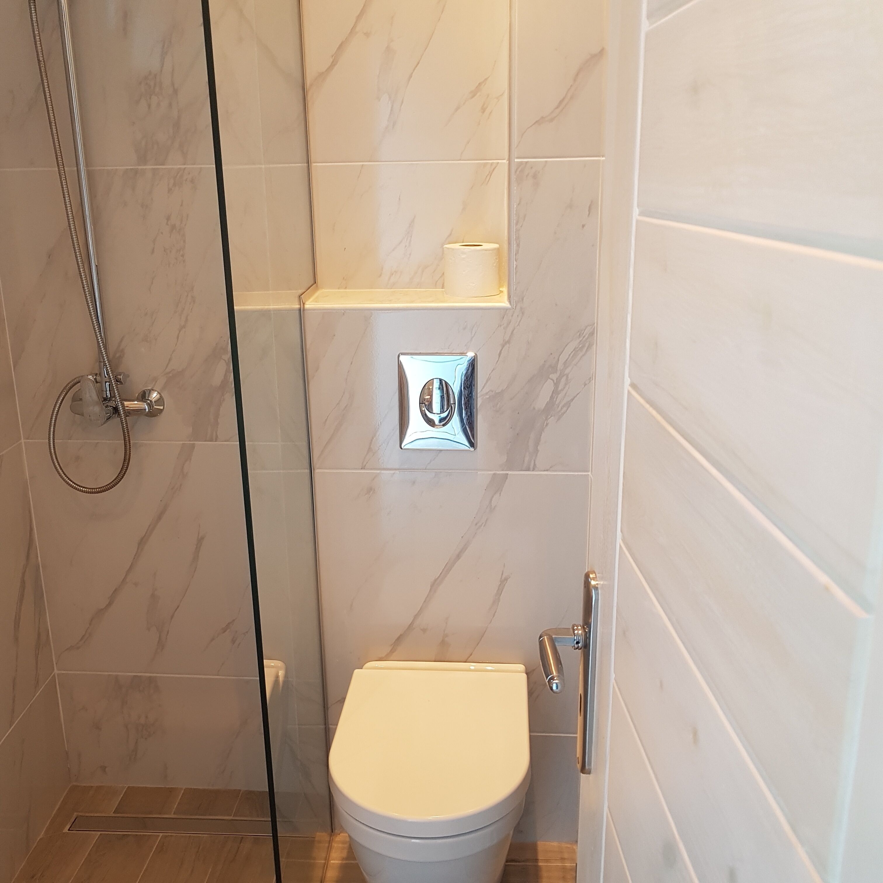A bathroom with a shower, toilet, and a shelf with a toilet paper holder.