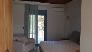 A bedroom with a bed, a chair, a window with curtains, and an air conditioning unit.
