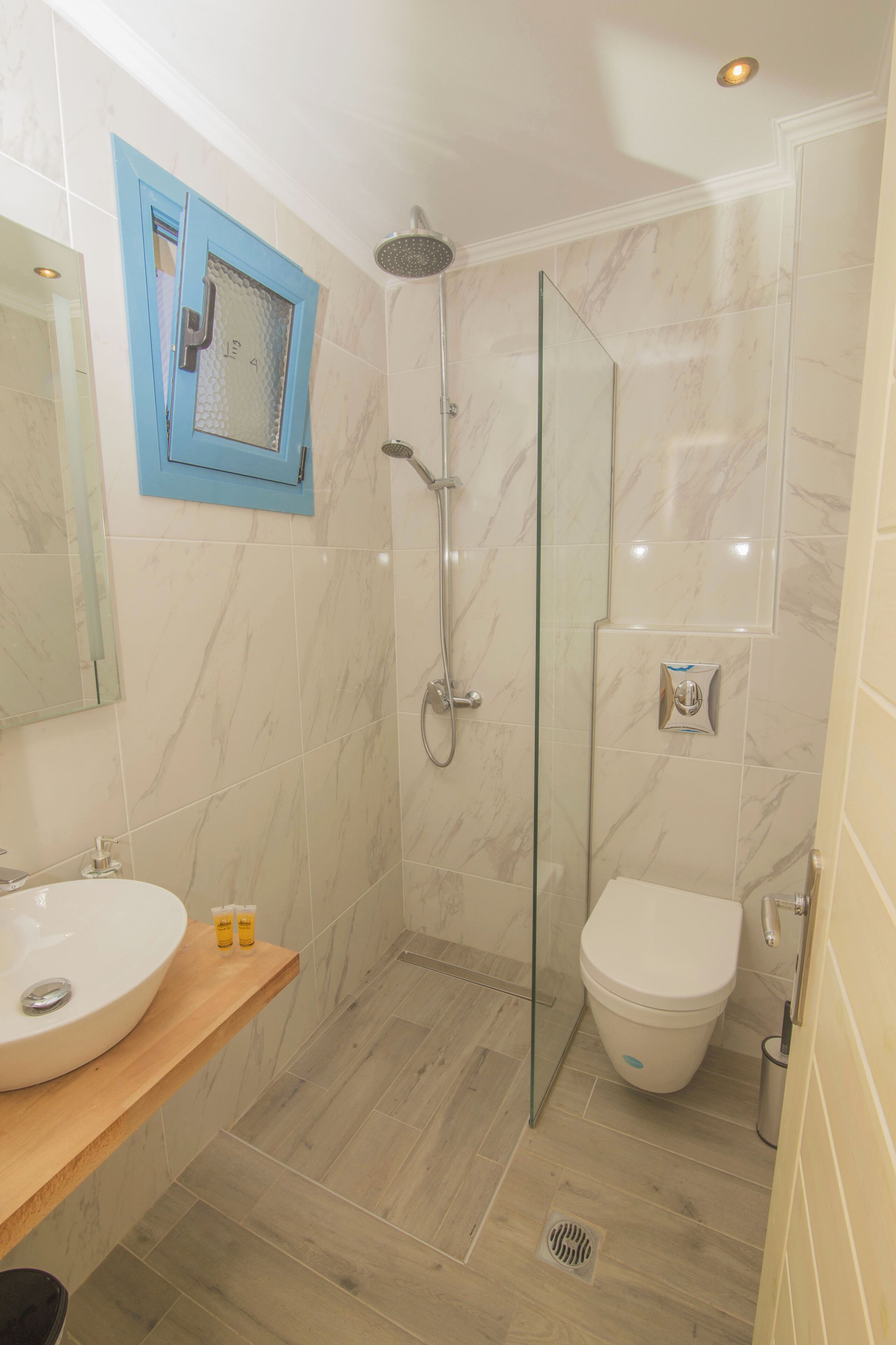 A modern bathroom with a glass shower enclosure, a white toilet, and a marble-tiled floor.