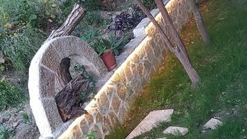 Un muro de piedra de contención con jardinera integrada, rodeado de césped y plantas pequeñas.