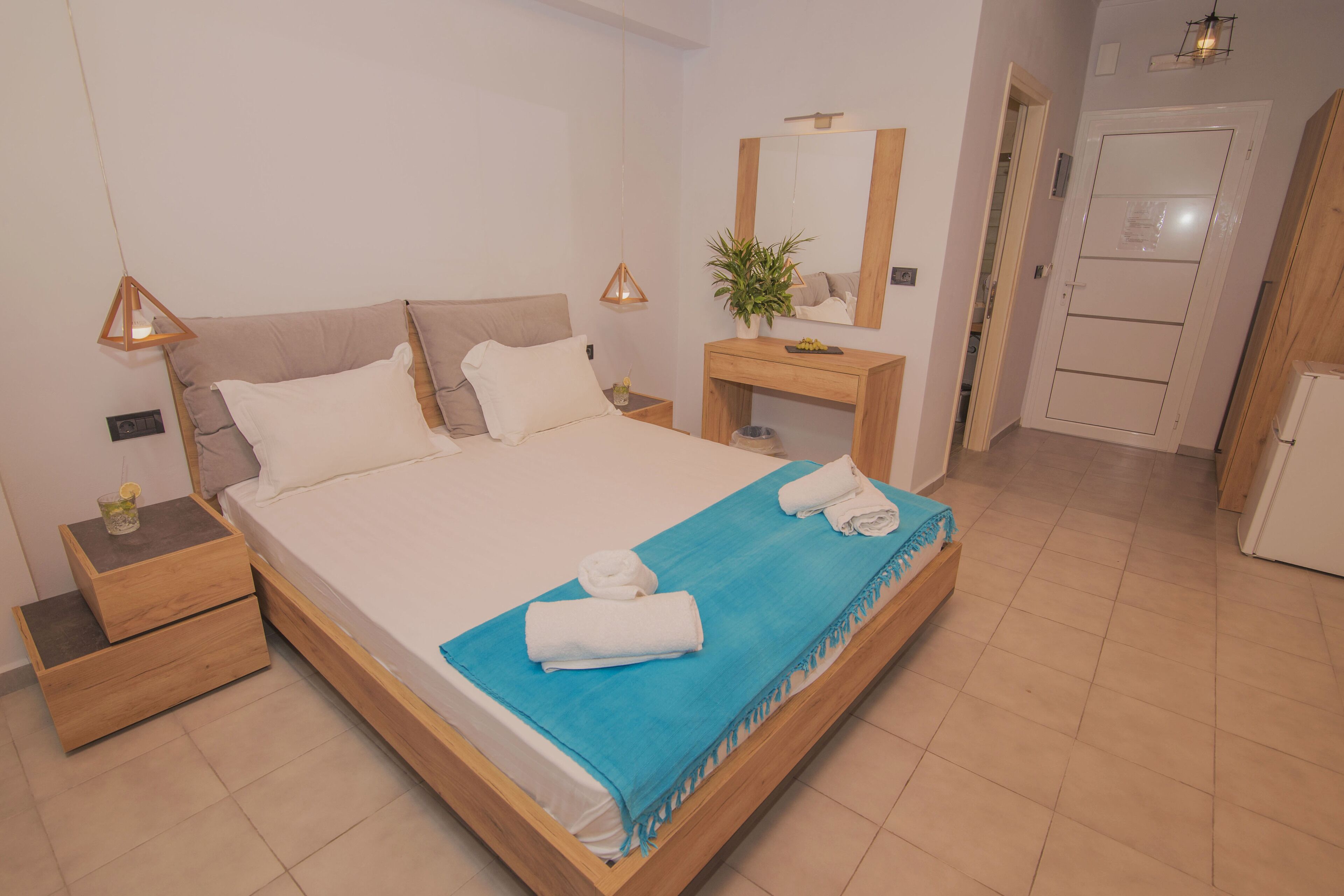 A neatly made bed with a blue towel, a wooden nightstand with a lamp, and a small table with a plant.
