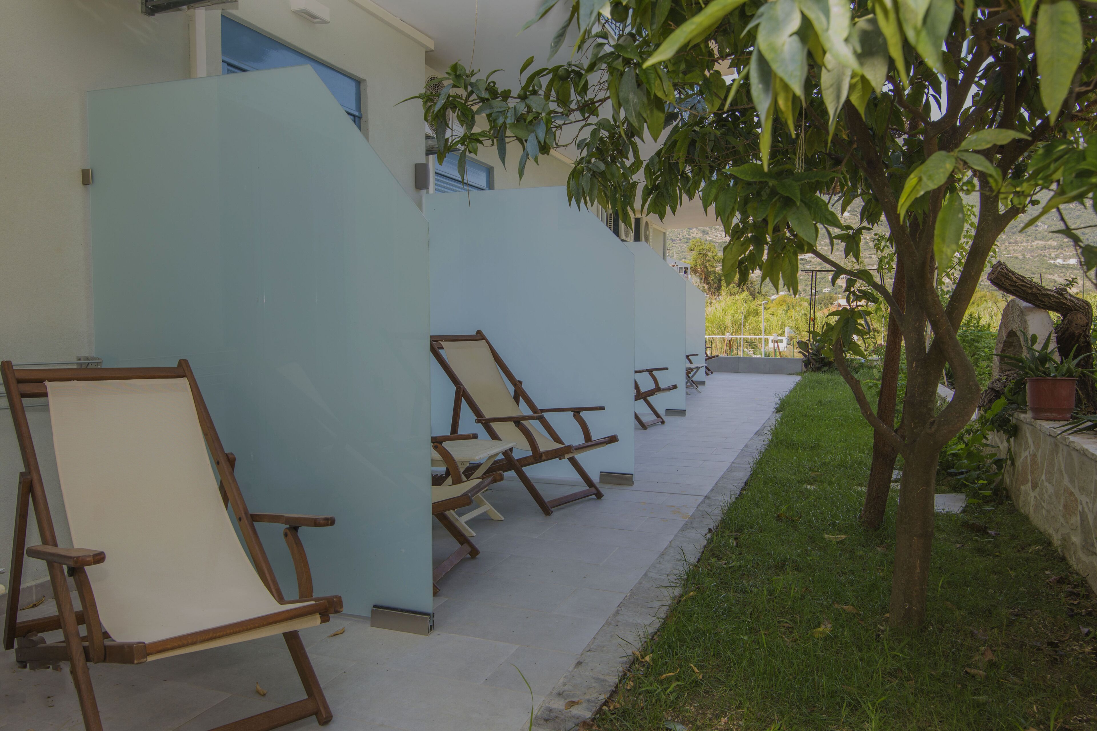 A covered outdoor seating area with wooden chairs and a table, surrounded by light blue walls and a small tree.