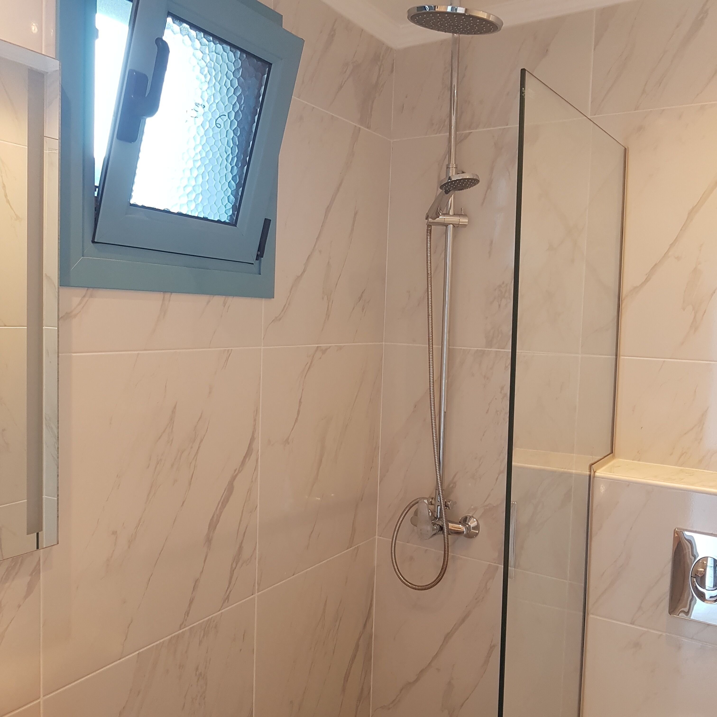 Une salle de bain moderne dotée d’une douche à parois de verre, d’un pommeau de douche à main et d’un robinet mural.