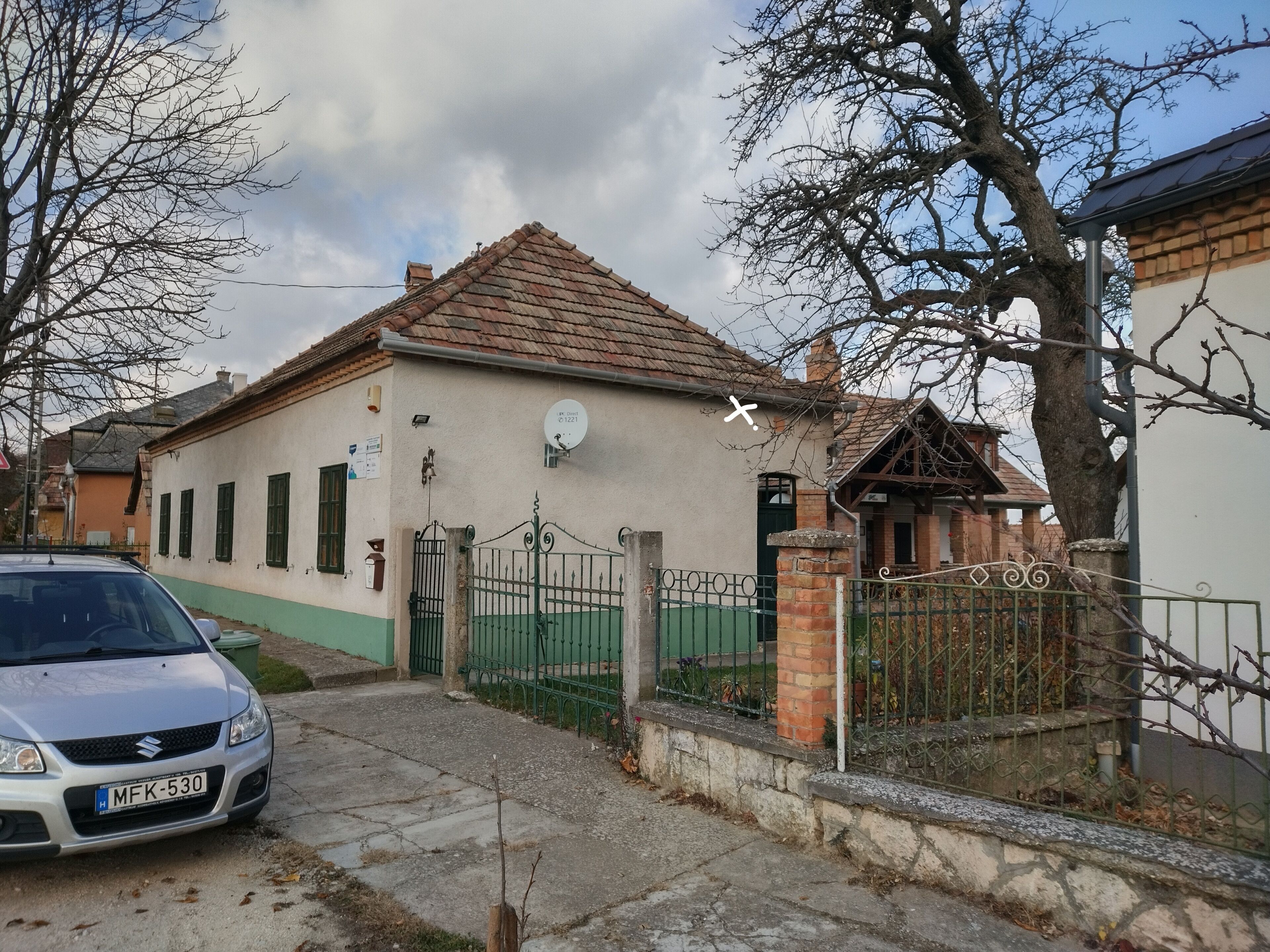 A residential building with a tiled roof, a gated entrance, and a parked car.