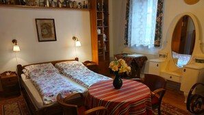 Une pièce comprenant un lit, des tables de chevet, une petite table avec un vase de fleurs, une chaise, un miroir et une étagère contenant divers objets.