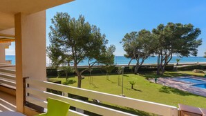 Ein Balkon mit Blick auf einen Swimmingpool, eine begrünte Fläche mit Bäumen und einem strahlend blauen Himmel.