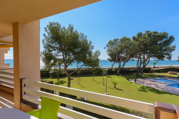 A balcony with a view of a swimming pool, a grassy area with trees, and a clear blue sky.