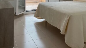 Ein Schlafzimmer mit Bett, Schreibtisch, Stuhl, einer Pendelleuchte und einer Glasgleittür zu einem Außenbereich.